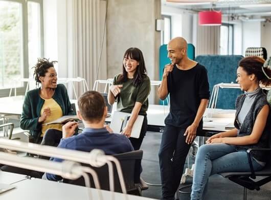 A group of people in a circle happily discuss something in the office.