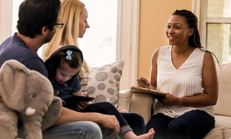 A female counsellor sitting on a chair with a clipboard, facing a couple with a child sitting on the man's lap | Master of Social Work (Qualifying)