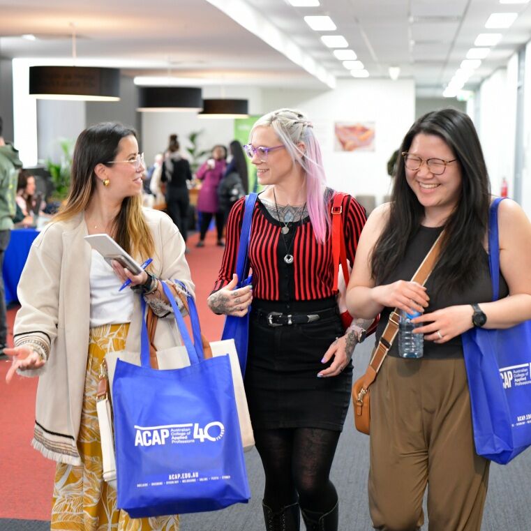Three females walking together and smiling at an ACAP info night event, wearing ACAP tote bags