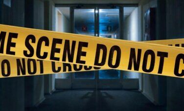 Crime Scene yellow tape is visible and featured across the image. "Crime Scene Do not cross" is printed in black on yellow tape. A glass double door is in the background. Dark shadows and backlight