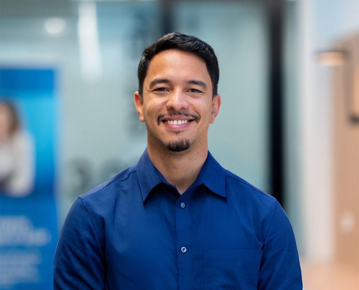 A male international student wearing a blue business shirt, standing at an ACAP campus and smiling towards camera (1224x990)