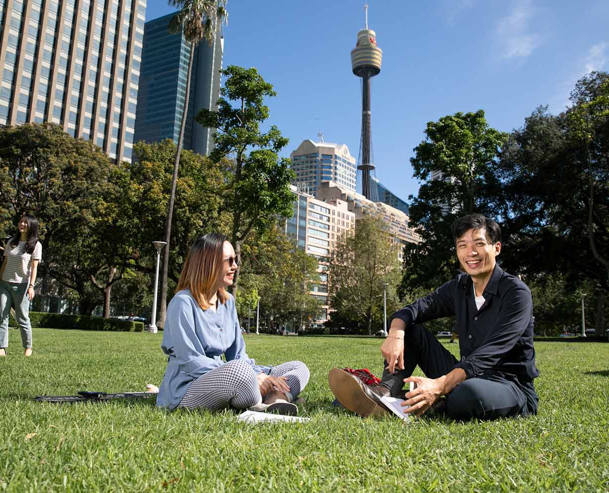 A female and male ACAP student sitting with notebooks in Hyde Park across the road from ACAP University College Sydney campus (1224x990)