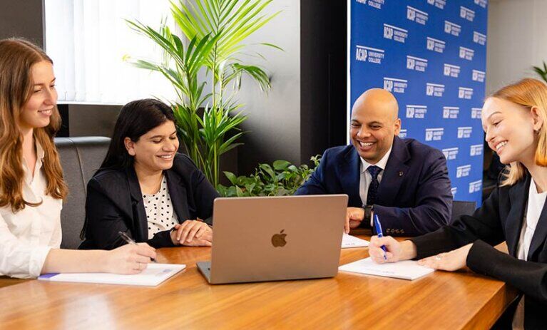 Four Law (PLT) students from ACAP University in Melbourne sitting around a desk in front of notepads and a laptop (828x676)
