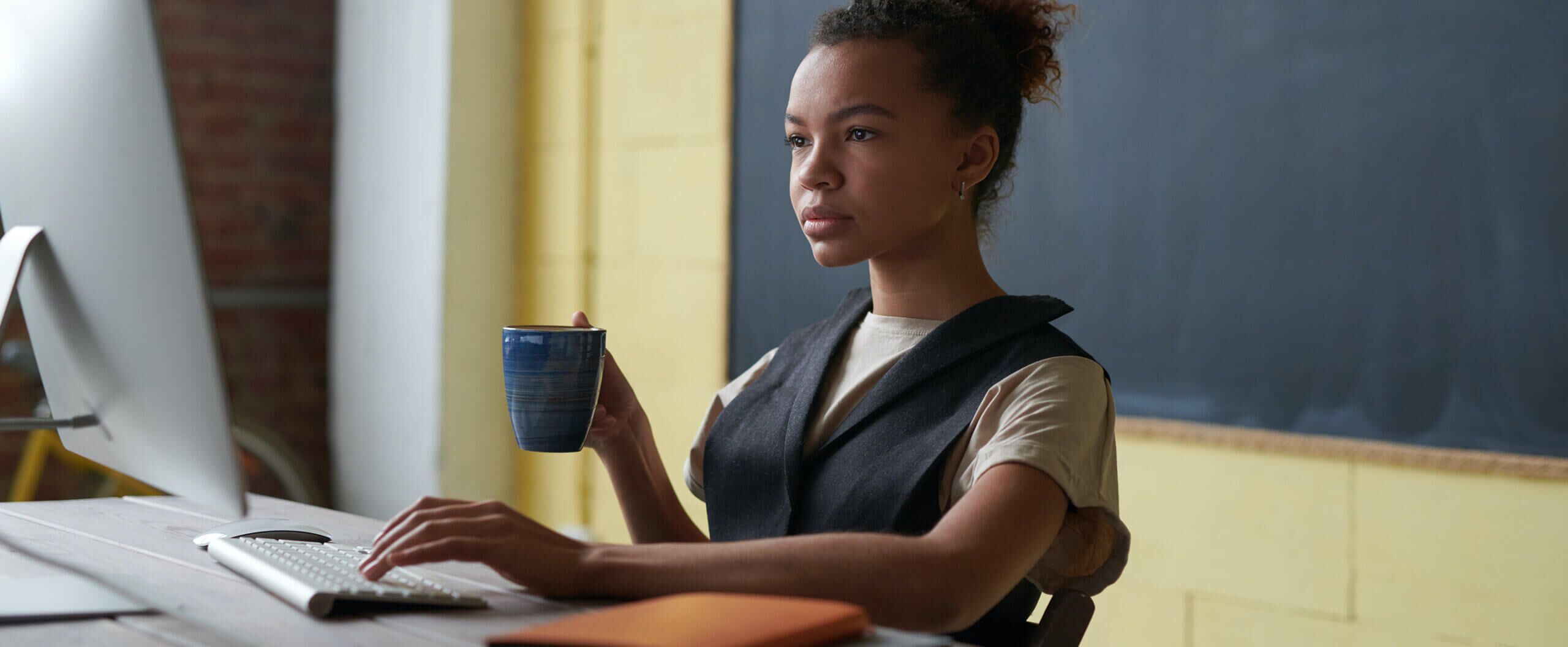 Student working on MAC holding a drink in a mug