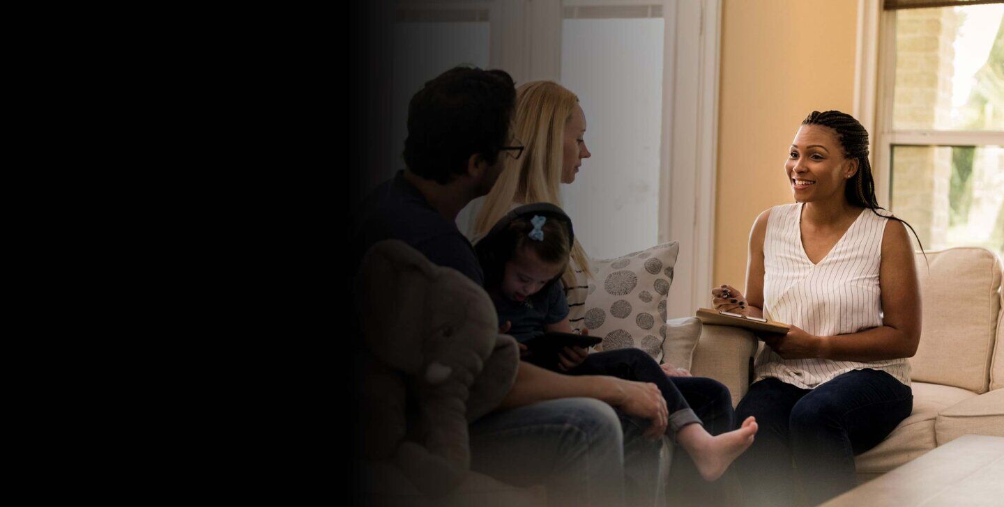 A female counsellor sitting on a chair with a clipboard, facing a couple with a child sitting on the man's lap | Master of Social Work (Qualifying)