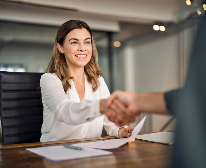 Young smiling woman sitting, shaking someone's hand over a work desk