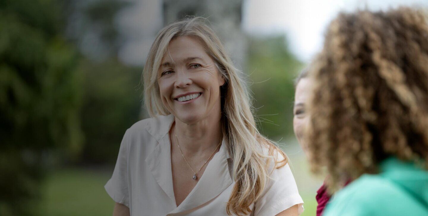 A woman with blonde hair smiling towards camera and standing with two other women - ACAP Counselling (1430x952)