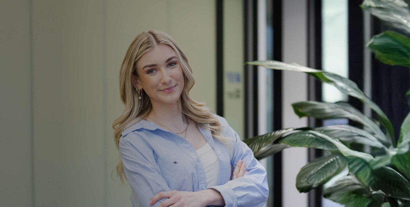 A woman with long blonde hair and earrings folding her arms and smiling towards a camera - ACAP Criminology (1430x952)