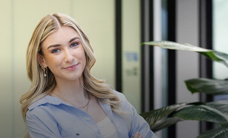 A woman with long blonde hair and earrings folding her arms and smiling towards a camera - ACAP Criminology (761x761)