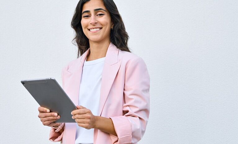 Woman stands in a pink jacket. With device.
