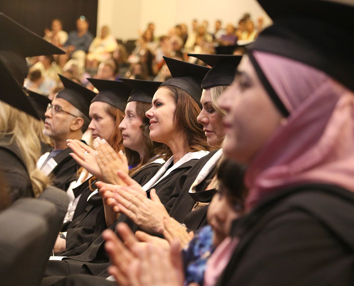 Six college graduates sitting in a row at an ACAP University College graduation ceremony, wearing graduation hats and robes (1224x990)