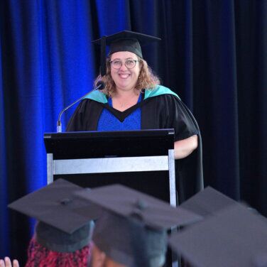 A recent ACAP graduate standing on stage in front of a lectern at an ACAP graduation ceremony (752x752)
